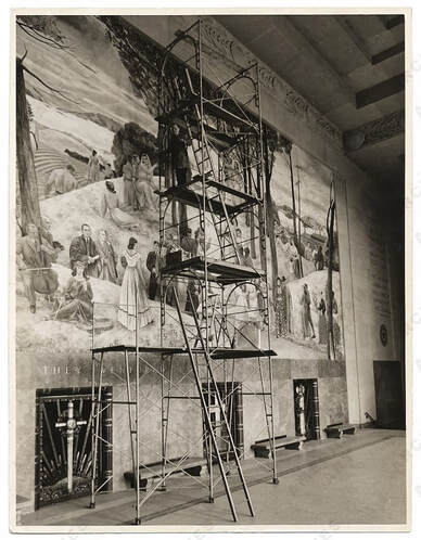 Photograph of Leon Kroll standing on a scaffold painting the center mural at the Worcester Memorial Auditorium.