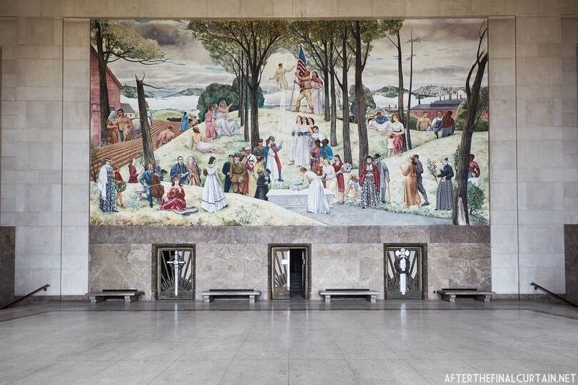 Photo of Leon Kroll's Shrine of the Immortal mural at the Worcester Memorial Auditorium. Mural depicts a WWI soldiers ascending to heaven while people place a wreath on his grave, sing hymns, and play music. In the background are historical scenes of Worcester's evolution from agricultural village to industrial city.